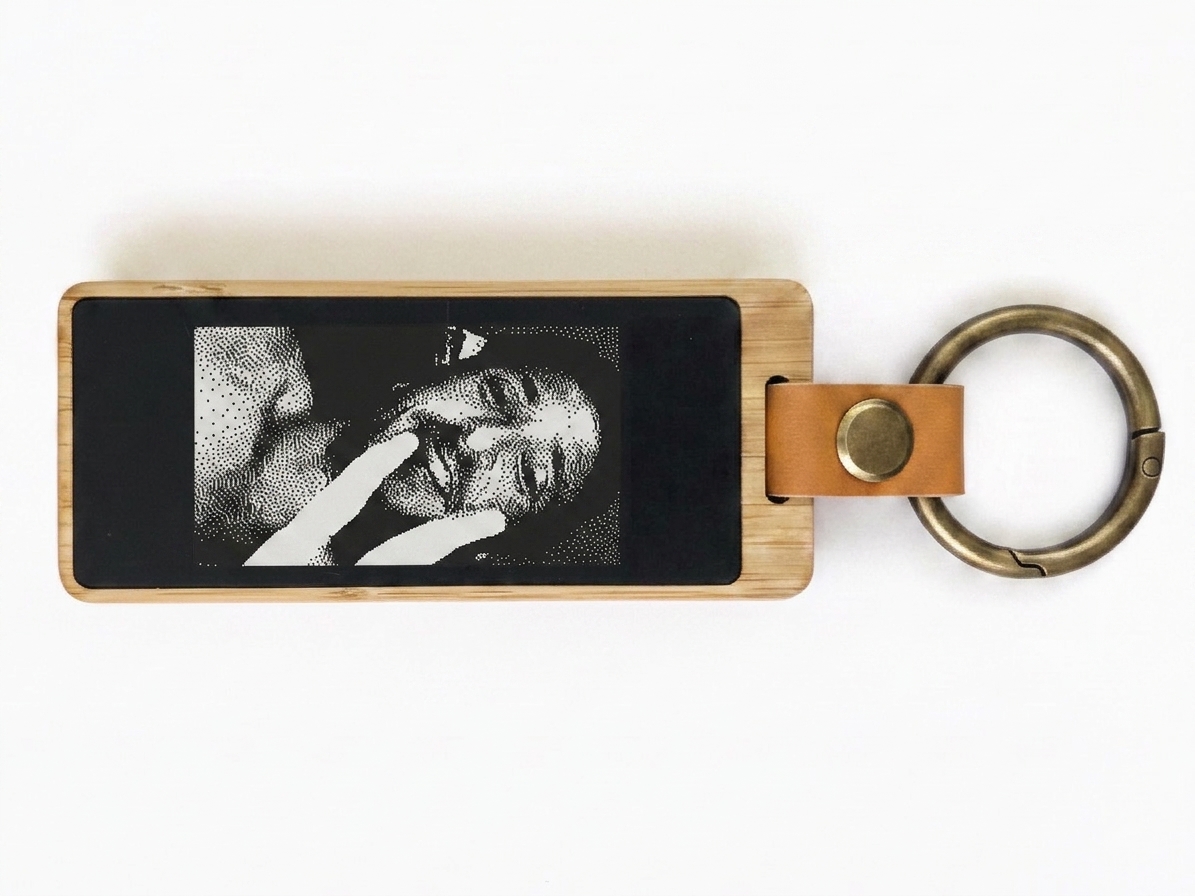 Un porte-clés KEEP, écran e-ink affichant un KEEPmoji — un selfie en noir et blanc tramé d'un couple.