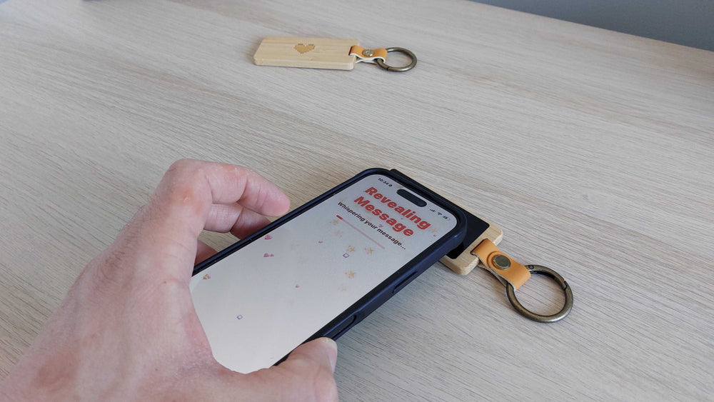 A hand holding a phone to a KEEP keychain on a desk, the phone screen reading Revealing message.