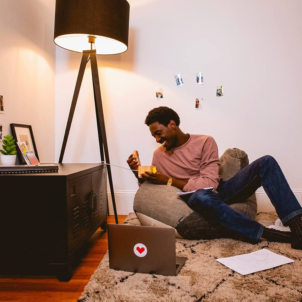 A young man laughing as he opens a Lovebox at home, a laptop with a pixel-heart sticker beside him.